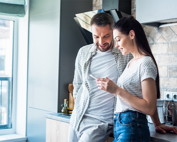 Smiling couple using smartphone together in kitchen, smart home concept