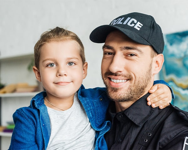 Happy young father in police uniform carrying his little son and looking at camera